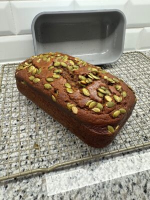 Pumpkin bread with pepita topping cooling on a rack next to a Caraway loaf pan