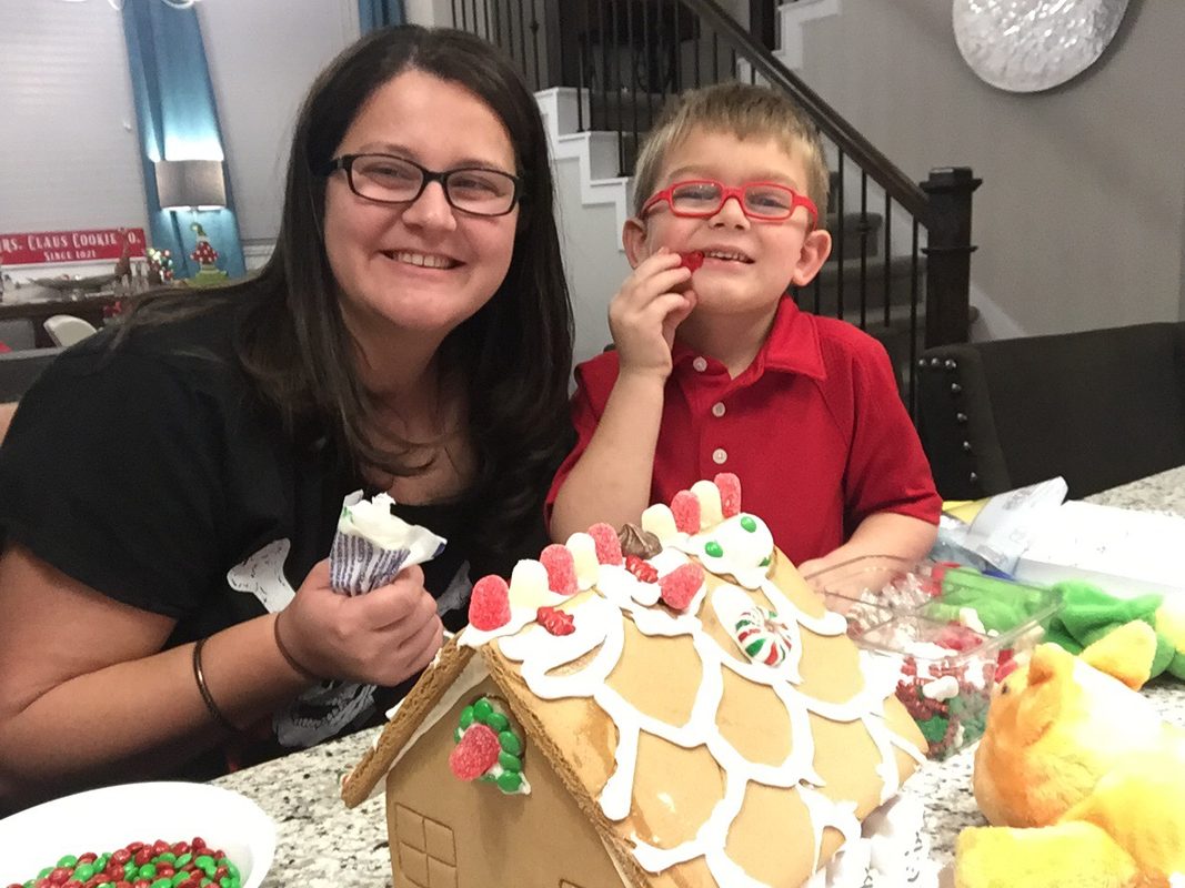 athy decorating a gingerbread house with her young son at their kitchen counter