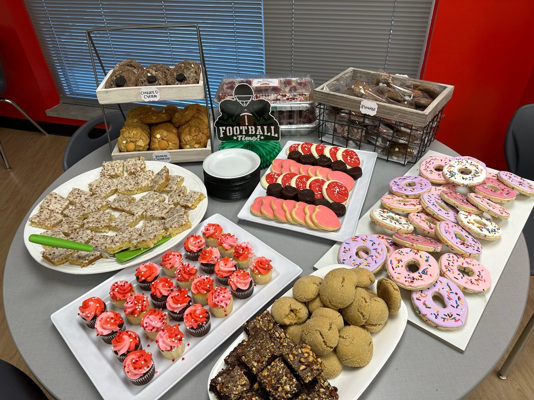 A football themed dessert table with cupcakes, sprinkled donut cookies, cookie bars, and trays of drop cookies made for a group event
