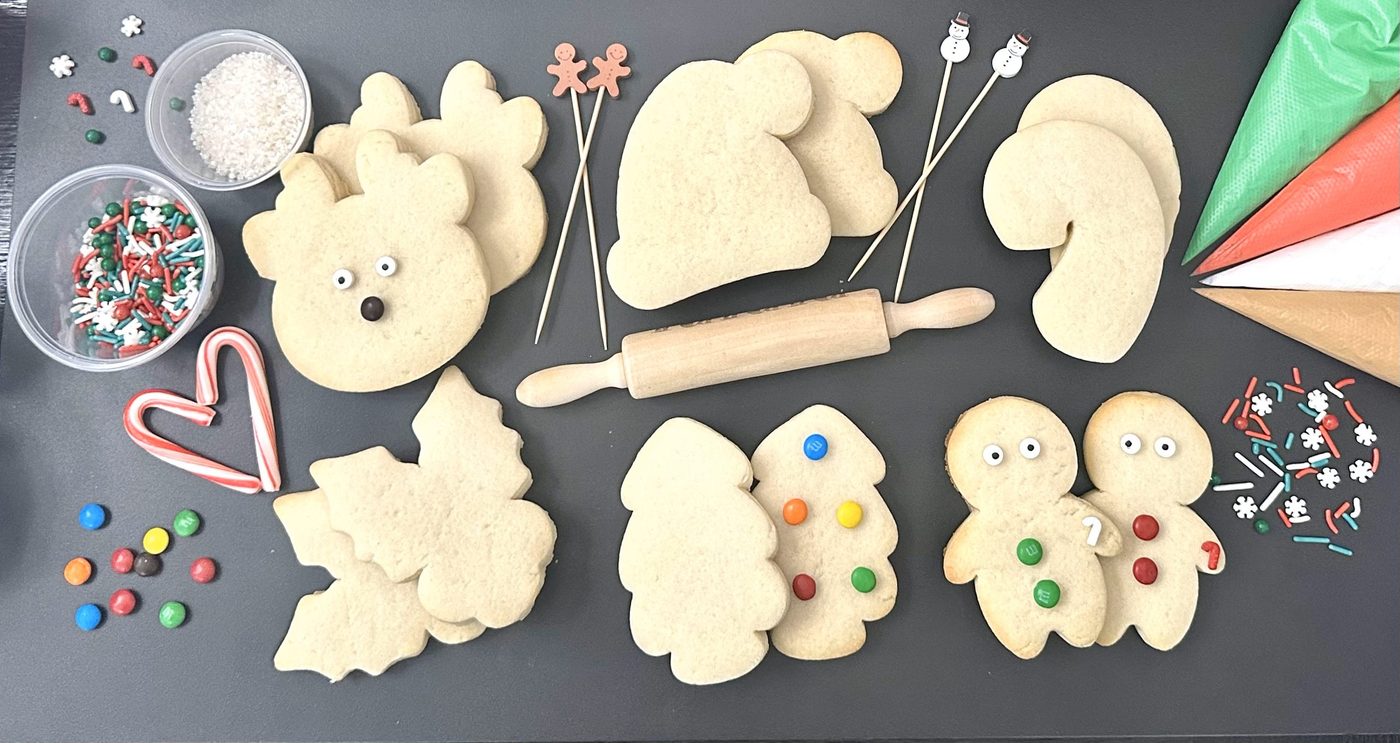 Kit contents flat lay: Christmas DIY cookie kit contents laid out — undecorated reindeer, tree, holly and candy cane sugar cookies with icing bags, sprinkle cups, candy eyes and cookie picks, ready to box