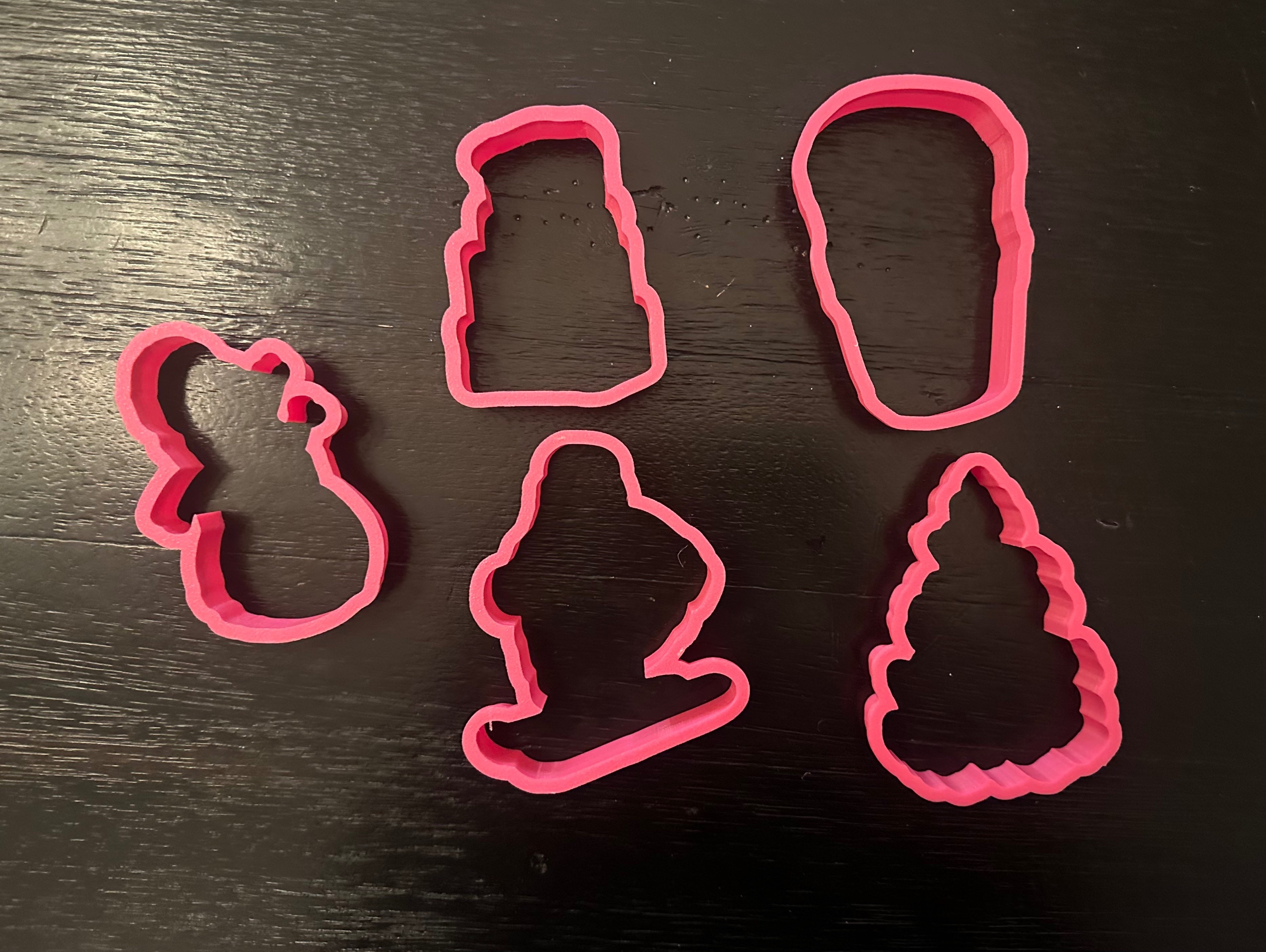 Five pink 3D printed cookie cutters in snowman, luggage, coffee cup, ski Santa and Christmas tree shapes
